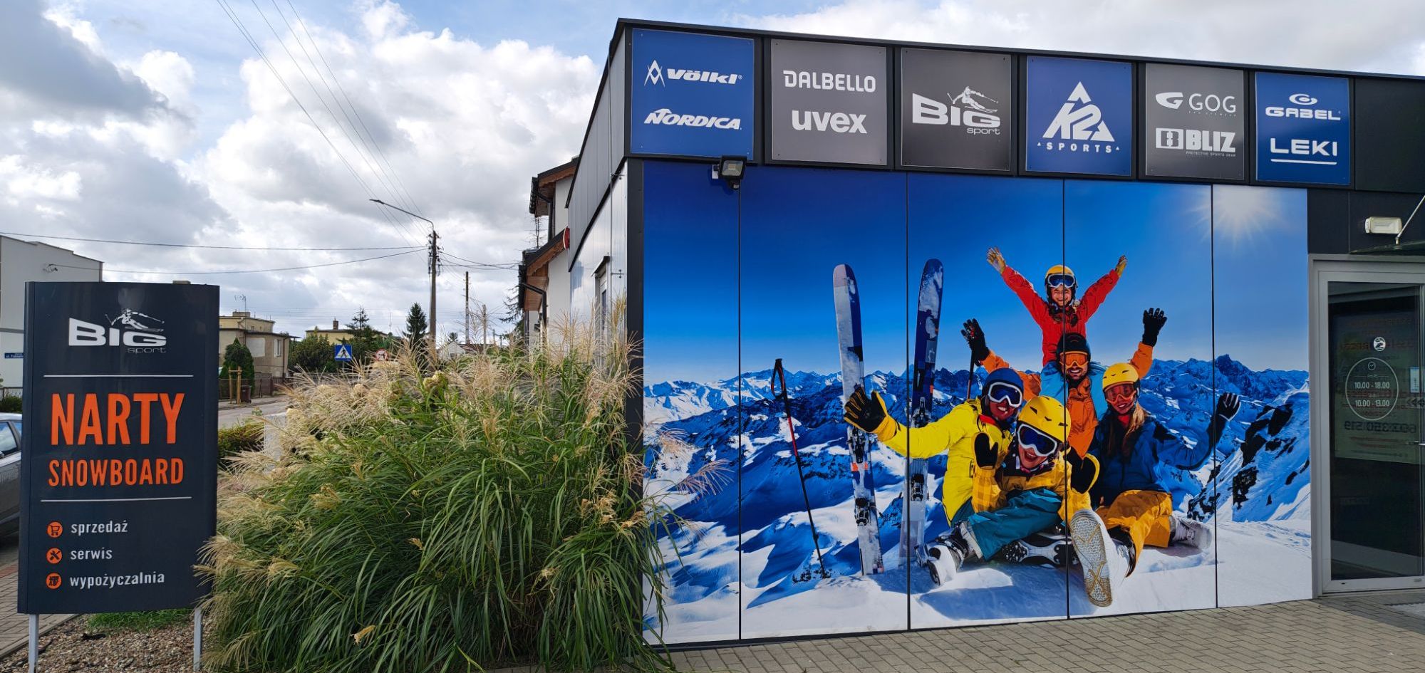 Sklep Big Sport w Kościanie: tablice z markami, mural z narciarzami i drzwi wejściowe